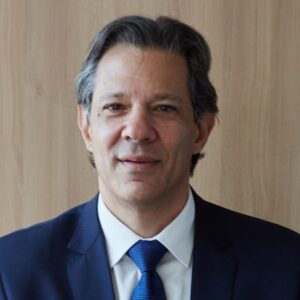 Fernando Haddad, de terno azul e gravata, posa para retrato com fundo neutro.